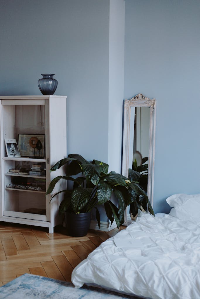 Sleeping Nook: 6 Sentuhan untuk Kenyamanan Maksimal di Kamarmu 6 Modern minimalist bedroom featuring a mirror, potted plant, and wooden cabinet for interior design inspiration.