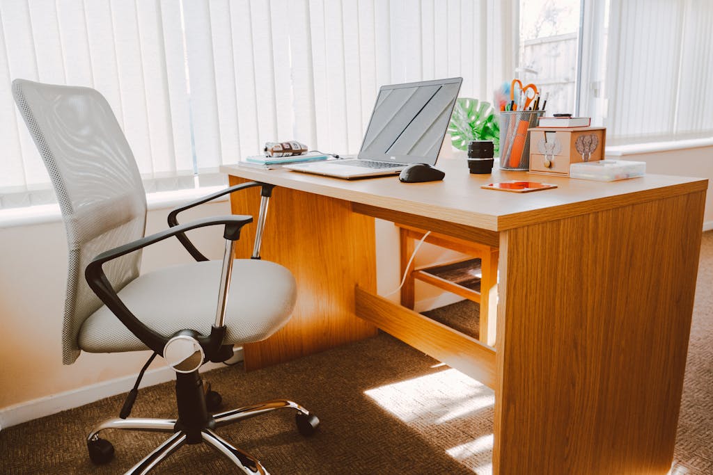 Cara Memilih Kursi Kerja untuk WFH 4 A modern office workspace featuring a wooden desk, chair, laptop, and bright natural light.