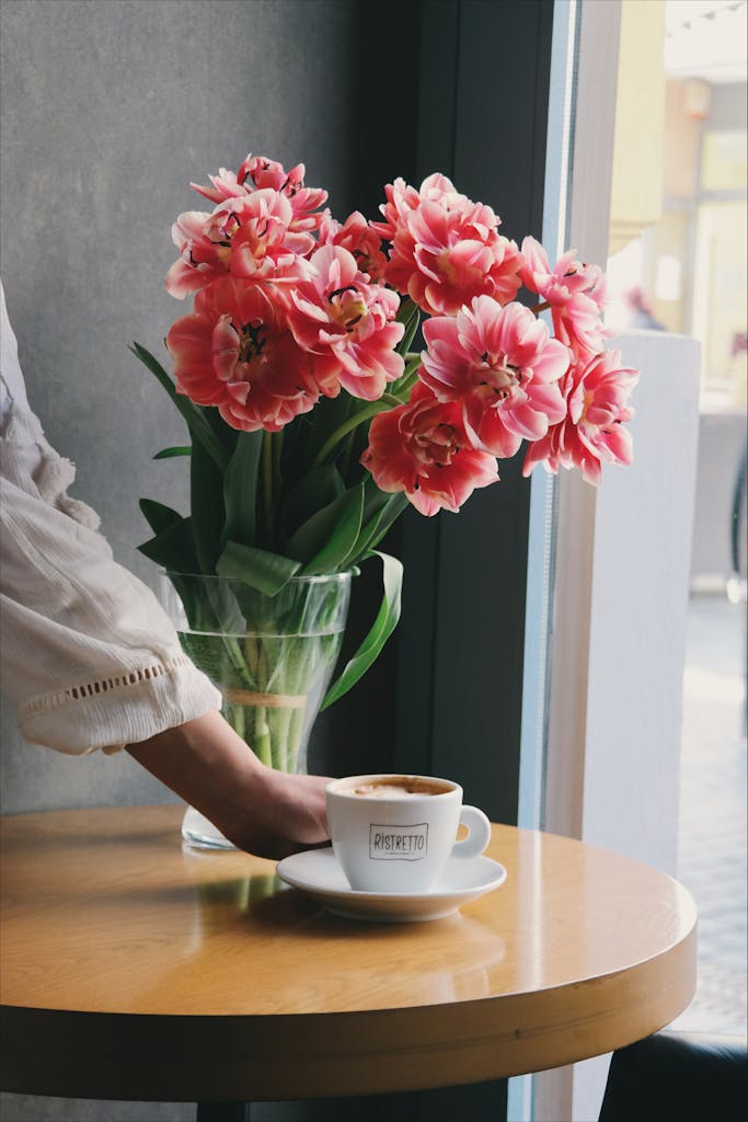 6 Trik Menata Coffee Table agar Terlihat Elegan dan Tidak Berlebihan 5 A serene indoor scene with fresh pink tulips in a vase beside a coffee cup on a wooden table.