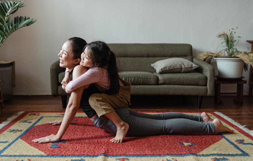 Mau Memilih Karpet? Ini 5 Hal Ini Wajib Kamu Tahu Agar Tidak Menyesal 6 A woman practicing yoga with her daughter in a cozy living room, embracing and smiling.
