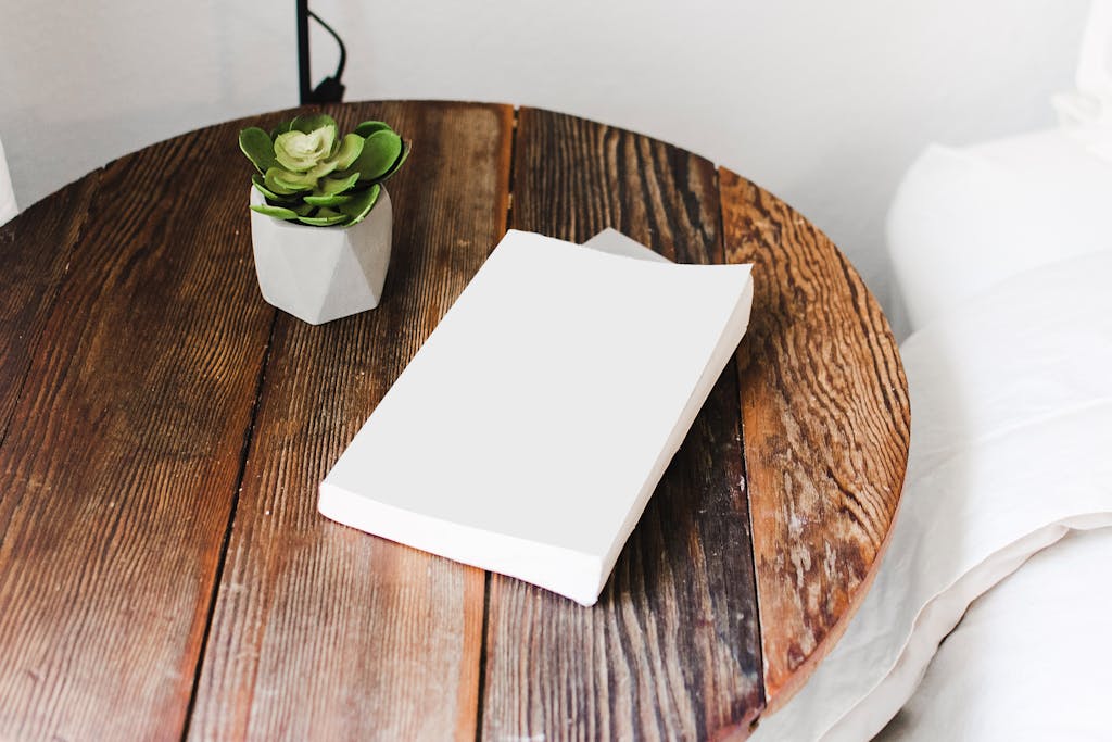 6 Trik Menata Coffee Table agar Terlihat Elegan dan Tidak Berlebihan 3 Close-up of a wooden bedside table with a succulent plant and a book, showcasing cozy home decor.