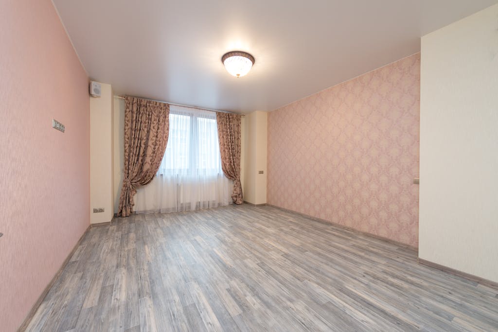 7 Cara Merawat Wallpaper Dinding agar Awet dan Warnanya Tetap Cerah 6 Empty spacious room with laminate and window with colorful curtains between walls with pink ornamental wallpapers and glowing white chandelier