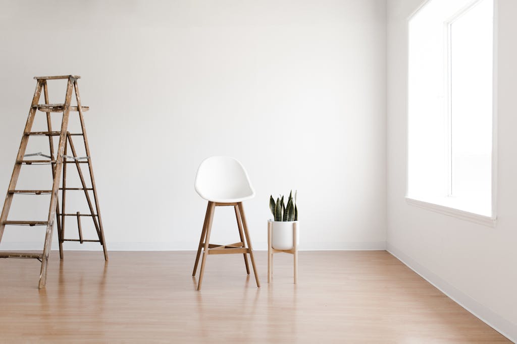 Investasi Interior: Ini Bagian Rumah yang Layak Dibayar Mahal 8 Minimalist interior featuring a white chair, wooden ladder, and snake plant by a window.