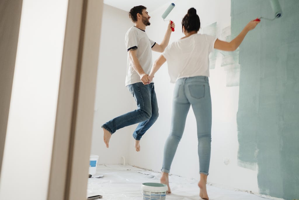 Panduan Lengkap Renovasi Kamar Tidur: Dari Perencanaan sampai Estimasi Biaya 3 A playful couple painting walls together in their home, having fun while holding hands.