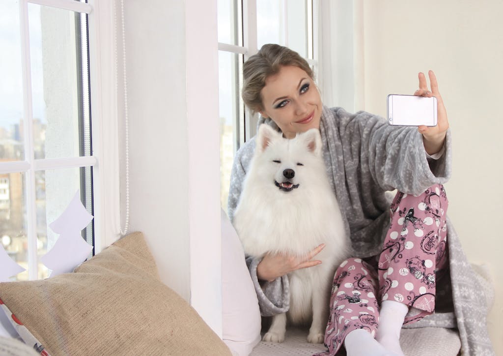 Rumah Pet Friendly yang Tetap Mewah, Desain Elegan Tanpa Kompromi 7 A woman in cozy pajamas takes a selfie with her fluffy white dog by the window, enjoying a relaxing morning.