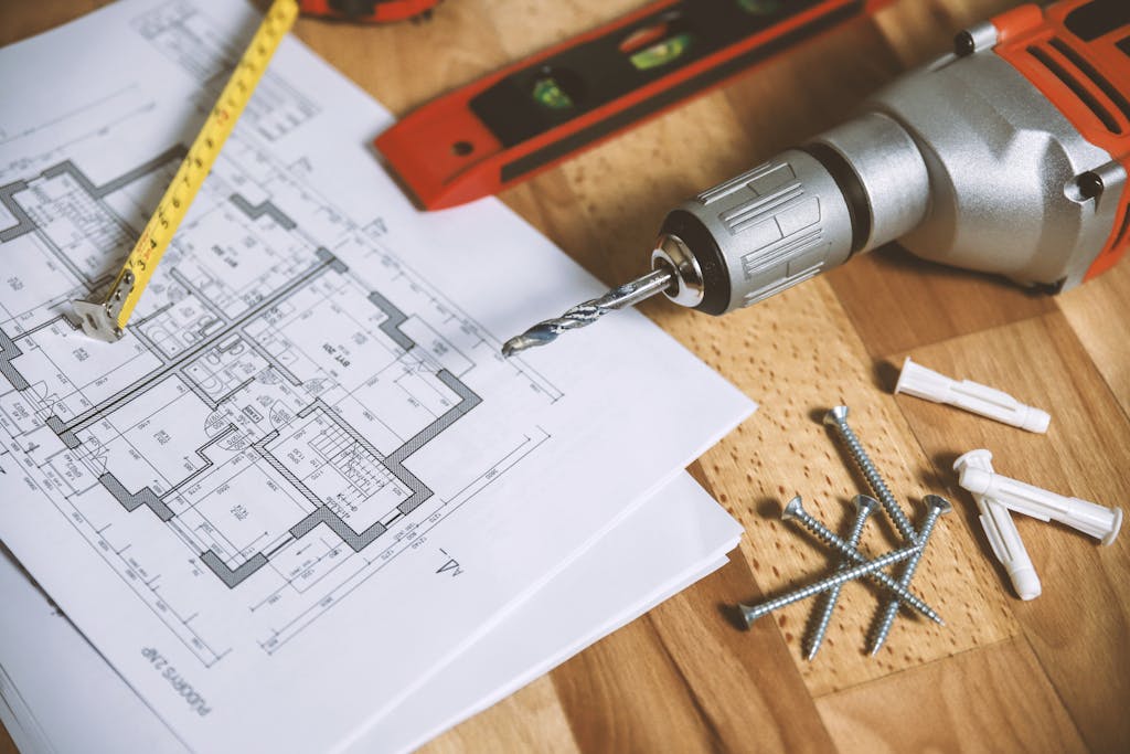 Panduan Lengkap Renovasi Kamar Tidur: Dari Perencanaan sampai Estimasi Biaya 2 Close-up of construction blueprint with tools like drill and screws on a wooden table.