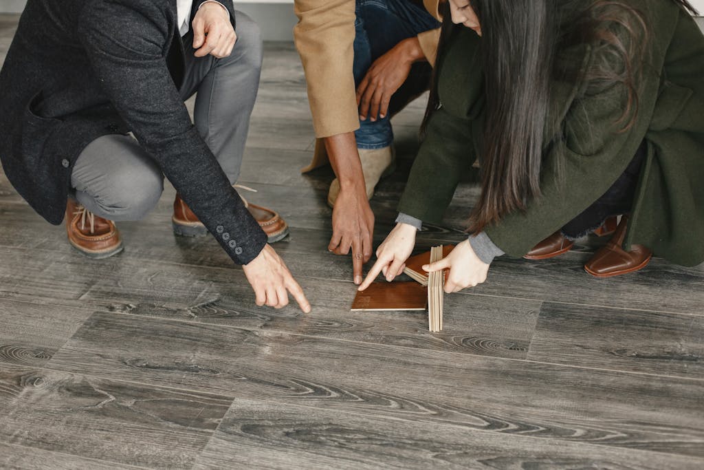 6 Pilihan Flooring Rumah yang Membuat Ruangan Terlihat Mewah 5 Three adults selecting flooring options indoors, focused on wooden samples and decision-making.