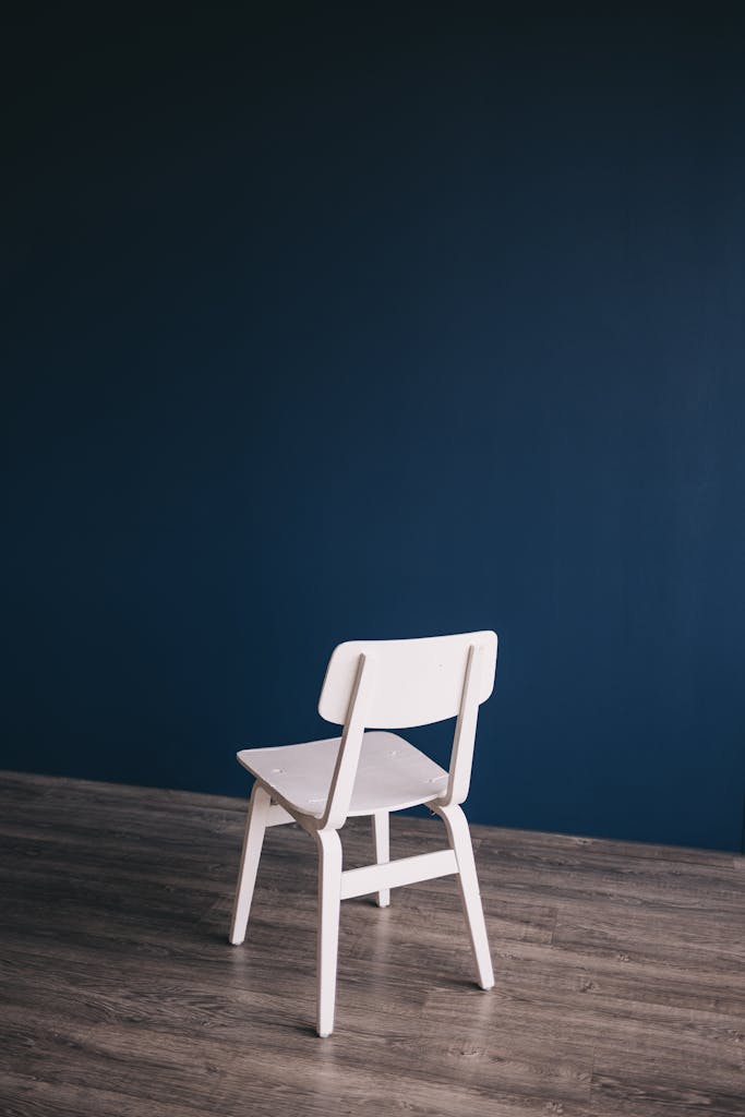 6 Pilihan Flooring Rumah yang Membuat Ruangan Terlihat Mewah 6 White chair on wooden floor with dark blue backdrop, perfect for modern interior design inspiration.